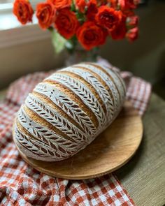 a loaf of bread sitting on top of a wooden plate next to a vase with red roses