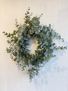 a wreath made out of eucalyptus leaves on a white wall with no one around it