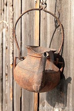 an old rusty kettle hanging on the side of a wooden fence