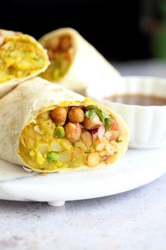 two burritos on a white plate with dipping sauce in the middle and one filled with chickpeas