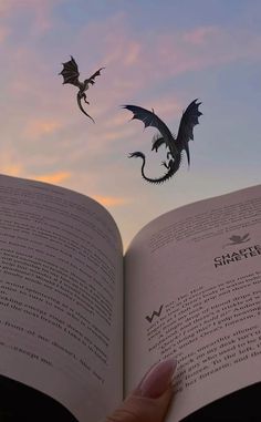 a person holding an open book in their hand and flying a paper dragon above them