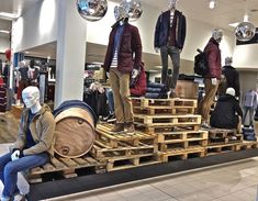 mannequins dressed in jackets and jeans sit on wooden pallets inside a store