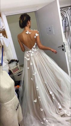 a woman in a white wedding dress looking at herself in the mirror with her back to the camera