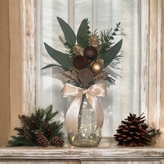 a vase filled with greenery sitting on top of a mantle next to pine cones