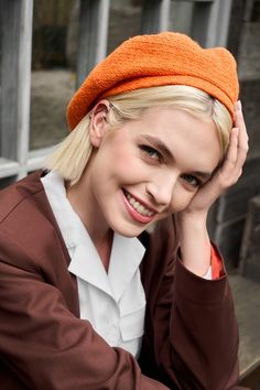 a woman with blonde hair wearing an orange headband and smiling at the camera while sitting on a bench