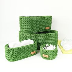 three green knitted baskets sitting next to each other on a white surface with cloths in them