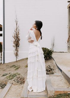 a woman standing in front of a white building wearing a dress with ruffles