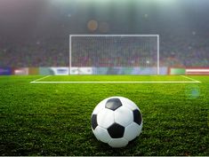 a soccer ball sitting on top of a lush green field in front of a stadium