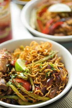 two bowls filled with noodles, meat and veggies on top of a table