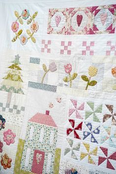 a close up of a quilt on a bed with flowers and houses in the background