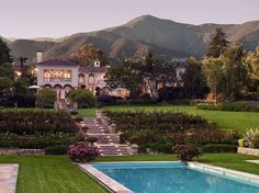 an outdoor swimming pool surrounded by lush green grass and trees with mountains in the background