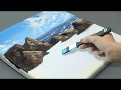 a hand is holding a paintbrush and painting a landscape on a piece of paper