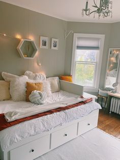 a white bed sitting in a bedroom next to a window covered in blankets and pillows