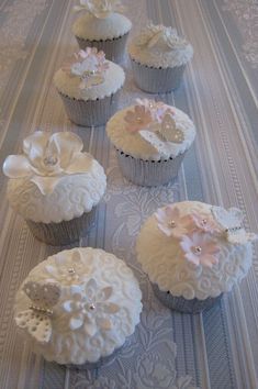 six cupcakes with white frosting and pink flowers on them sitting on a table