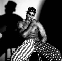 a shirtless man sitting in a chair with an american flag on the leg and his shadow behind him