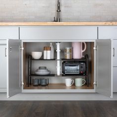 an open cabinet in the middle of a kitchen with coffee cups and other items on it