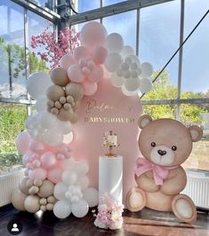 a teddy bear sitting in front of a balloon arch with flowers and balloons on it