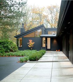 a black house with lots of windows and trees in the back ground, along with plants on either side