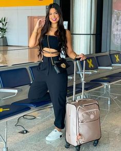 a woman standing next to an airport holding a suitcase and posing for the camera with her hand on her hip