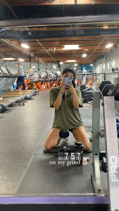 a woman sitting on the ground taking a selfie with her cell phone in a gym