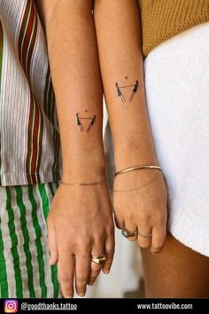 two people holding hands with tattoos on their arms and one has a small arrow in the middle