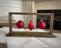 two red ornaments in a wooden frame sitting on a white blanket near a fire place