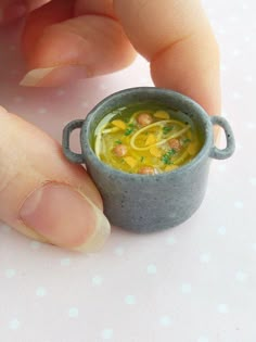 someone is holding a miniature bowl of soup in their hand and it looks like they are going to eat something out of the cup