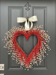 a heart - shaped wreath with white bows hangs on a door in front of a black door