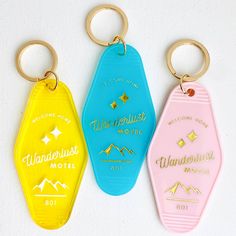 three different colored key chains with the words wanderluster motel on them and mountains in the background