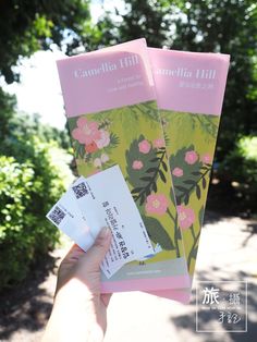 someone holding up two pamphlets in front of the camera with trees and bushes behind them