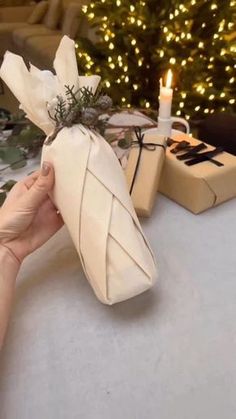 a person holding a wrapped present in front of a christmas tree with lights on it