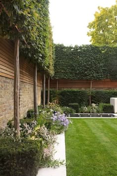 an outdoor garden with grass, shrubs and trees in the back yard area is well manicured