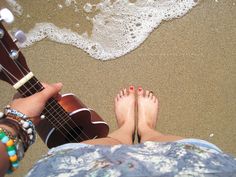 two people with their feet in the sand playing guitar