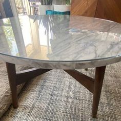 a marble table with wooden legs on carpeted floor next to planter and window