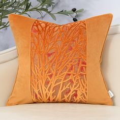 an orange pillow on a white couch next to a potted plant