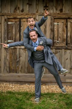 two men in suits are playing with each other on the grass near a wooden building