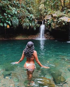 a woman standing in the water near a waterfall