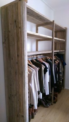 an open closet with clothes hanging on wooden shelves