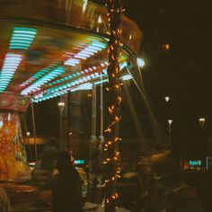 a merry go round ride at night with people walking around the area and lights on it