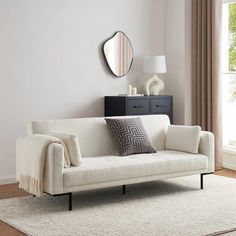 a living room with a white couch, mirror and rug on the floor in front of it