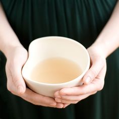 a woman holding a white bowl filled with liquid in her hands, while wearing a green dress