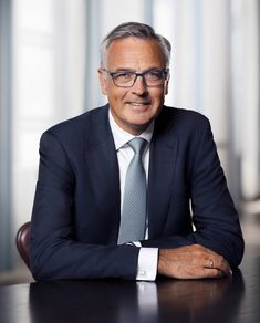 a man in a suit and tie sitting at a table with his arms folded out