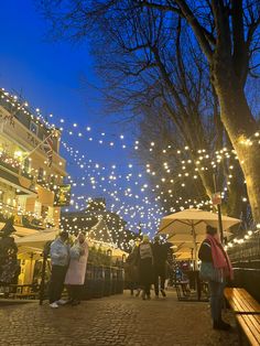 many people are walking down the street with umbrellas and christmas lights strung over them