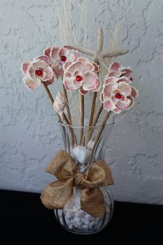 a vase filled with pink flowers and seashells on top of a black table