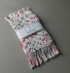 a white and red knitted scarf on top of a gray table with a tag