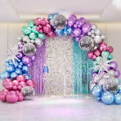 an arch made out of balloons and streamers in the middle of a white room