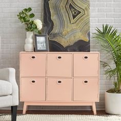 a living room with a white chair and a pink cabinet in front of a brick wall