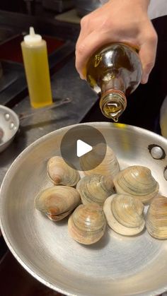 a person pouring oil on some clams in a pan