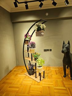 a cat statue sitting on top of a wooden floor next to a shelf filled with potted plants