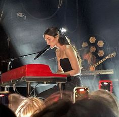 a woman standing at a red piano in front of a microphone and some other people